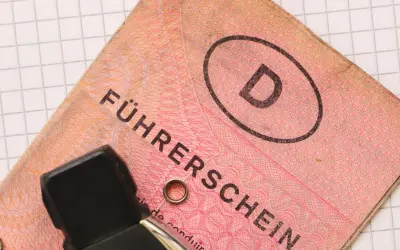Niemieckie prawo jazdy "Führerschein" z literą "D" w owalu, na tle kratkowanej kartki.
