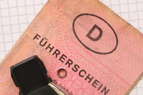 Niemieckie prawo jazdy "Führerschein" z literą "D" w owalu, na tle kratkowanej kartki.