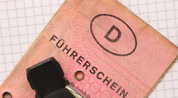 Niemieckie prawo jazdy "Führerschein" z literą "D" w owalu, na tle kratkowanej kartki.