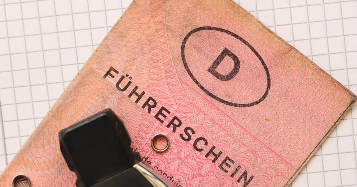 Niemieckie prawo jazdy "Führerschein" z literą "D" w owalu, na tle kratkowanej kartki.